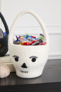 White felt skull-shaped basket with Halloween candy on a table.