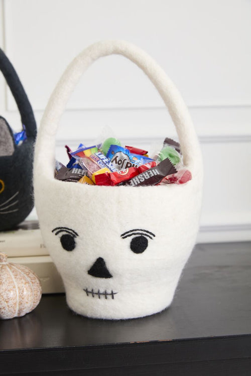 White felt skull-shaped basket with Halloween candy on a table.