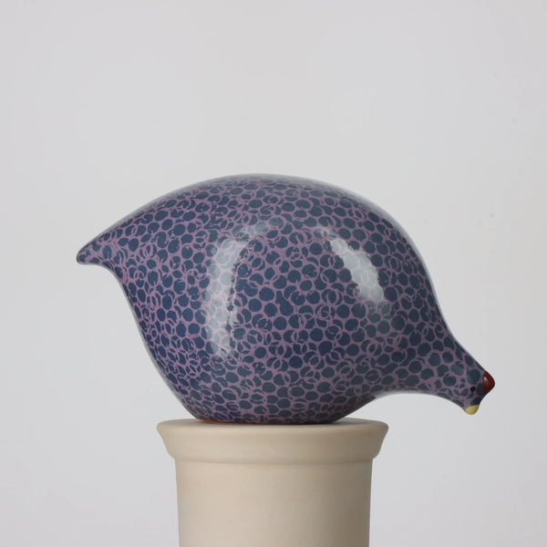 Ceramic pecking quail with blue and mauve pattern on a beige stand against a light gray background