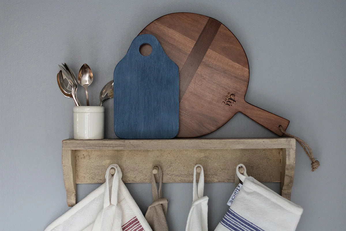 Wooden shelf with cutting boards, utensils, and hanging towels against a gray wall.