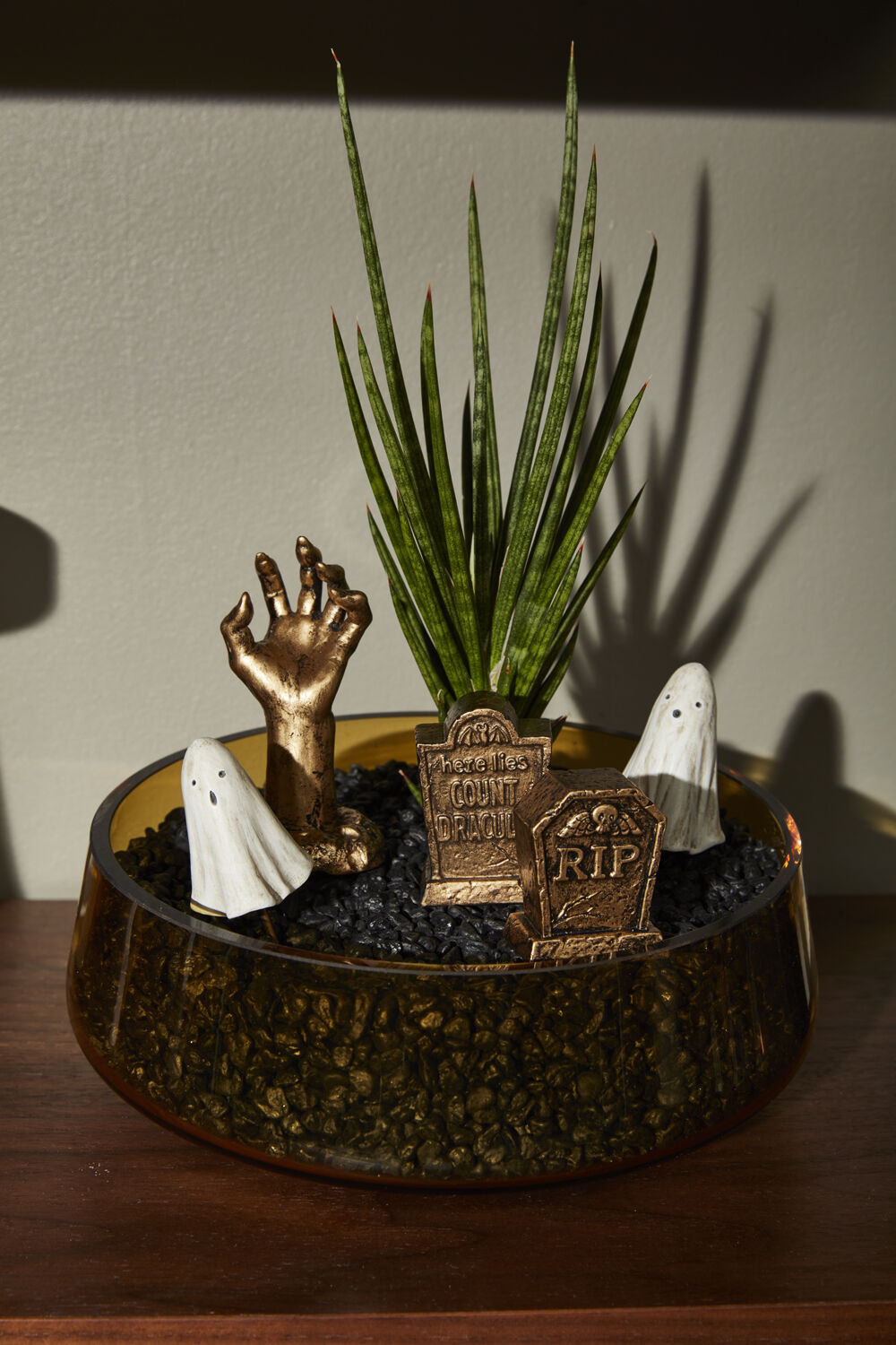 Decorative arrangement with a hand, ghosts, and tombstones in a pot on a wooden surface.