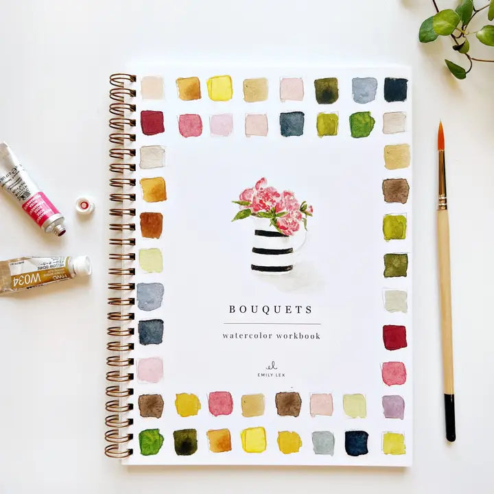 Watercolor workbook titled 'Bouquets' with color swatches on a white surface, surrounded by art supplies.