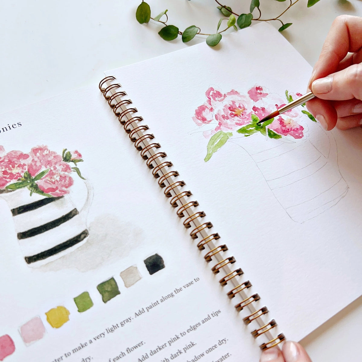 Person painting flowers in a notebook with a paintbrush