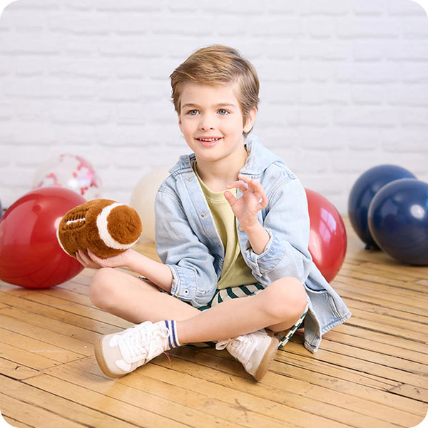 Child sitting on a wooden floor holding a plush toy with colorful balloons in the background.