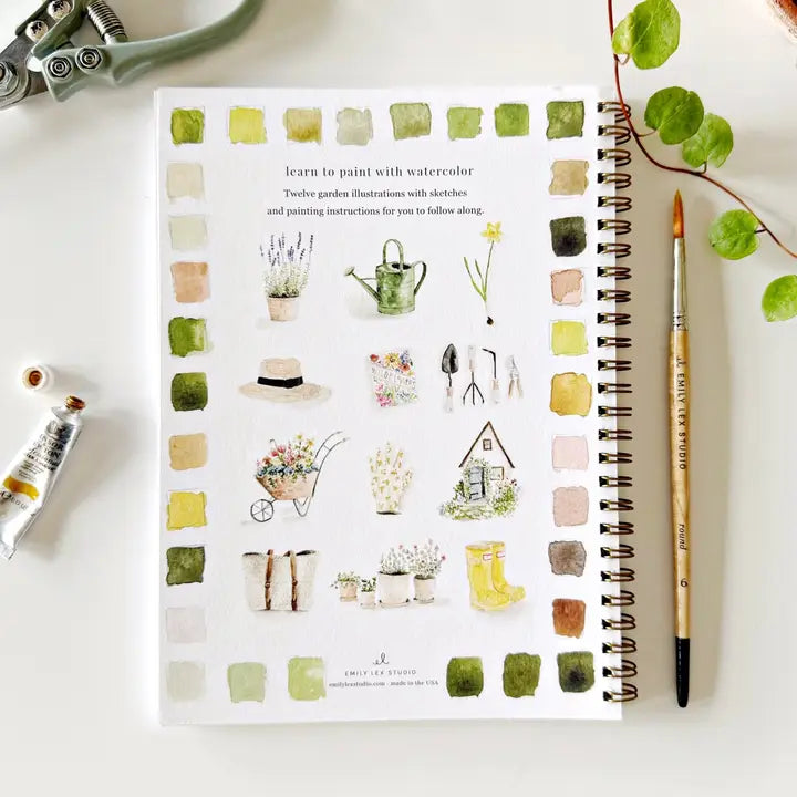 Notebook with watercolor illustrations of garden scenes on a white surface with art supplies.