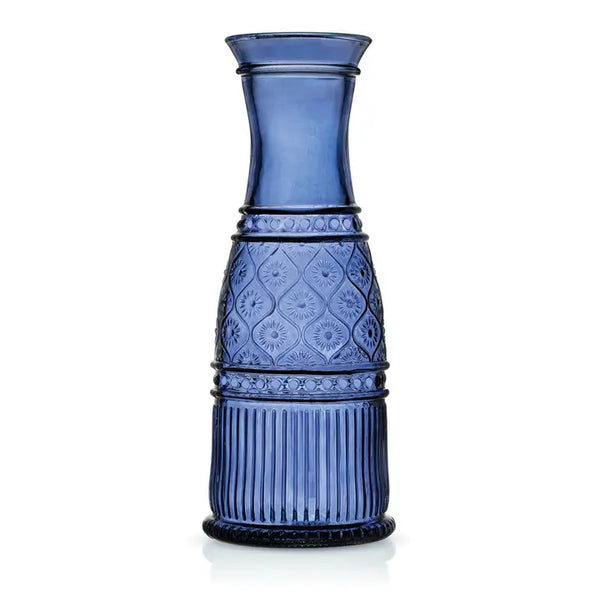 A cobalt blue glass carafe with a flared rim, textured diamond pattern on the middle section, and vertical fluting near the base, shown on a white background.