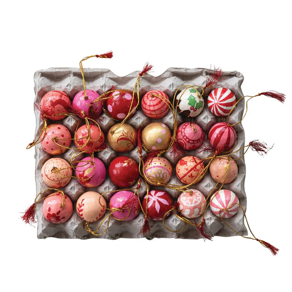 Decorative handmade paper maiche Christmas ornaments in an egg carton on a white background