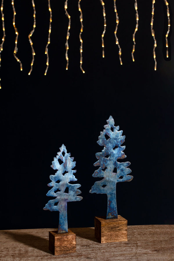 Two blue decorative trees on wooden stands with string lights in the background.