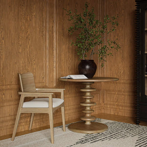 A circular accent table in a room with a plant on book on top of it next to a chair.