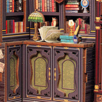 A miniature bookcase and cabinet unit in a detailed library setting, featuring dark wood panels with green patterned glass doors, surrounded by miniature books, a stained-glass lamp, an open book, and a small owl figurine.