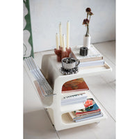 White shelf with books, candles, and decorative items on a light gray surface.