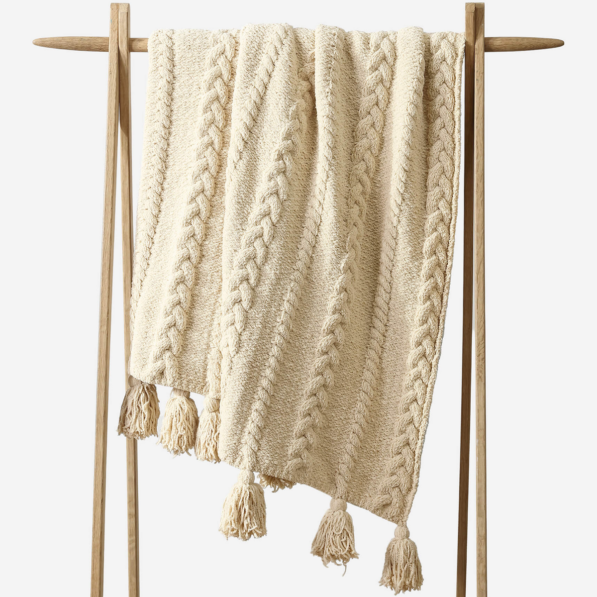 Beige knitted blanket with tassels on a wooden stand against a white background