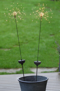 Decorative solar starburst stake lights in a pot on a wooden surface with a grassy background