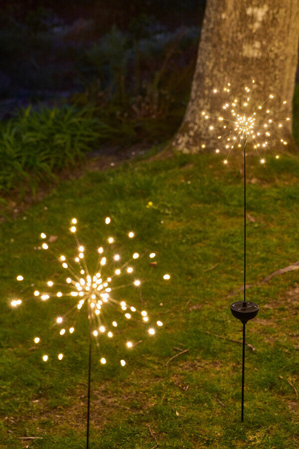 Decorative outdoor lights on grass with a tree in the background