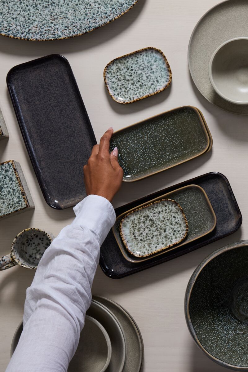 Hand interacting with ceramic plates and trays on a light surface