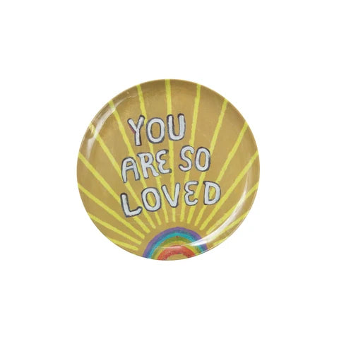 Round melamine plate with 'You are so loved' text and rainbow design on a yellow background