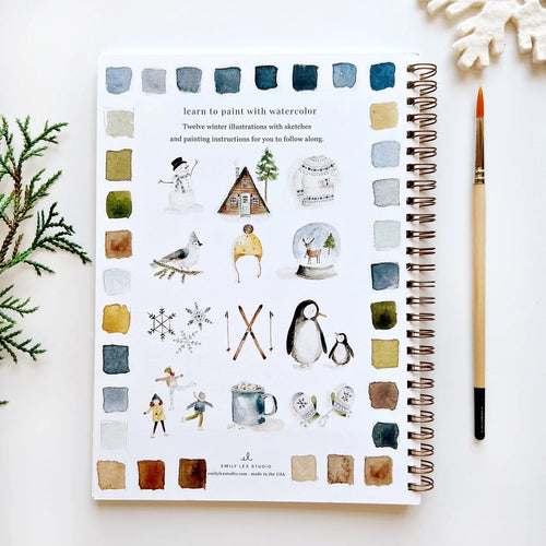 Illustrated book with winter-themed illustrations and a paintbrush on a white surface.