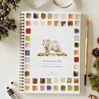 Woodland watercolor workbook with a bear illustration on a white surface with decorative items.
